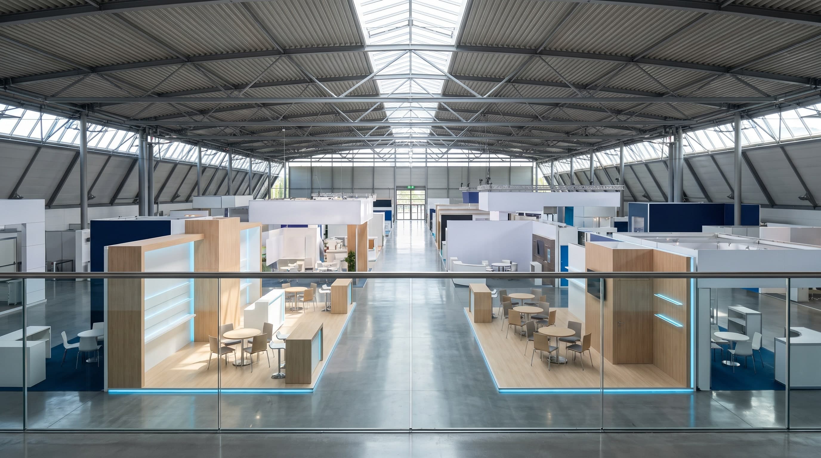 Blick von einer Galerie in eine weite Messehalle mit Ständen und Besprechungsinseln, ohne Menschen